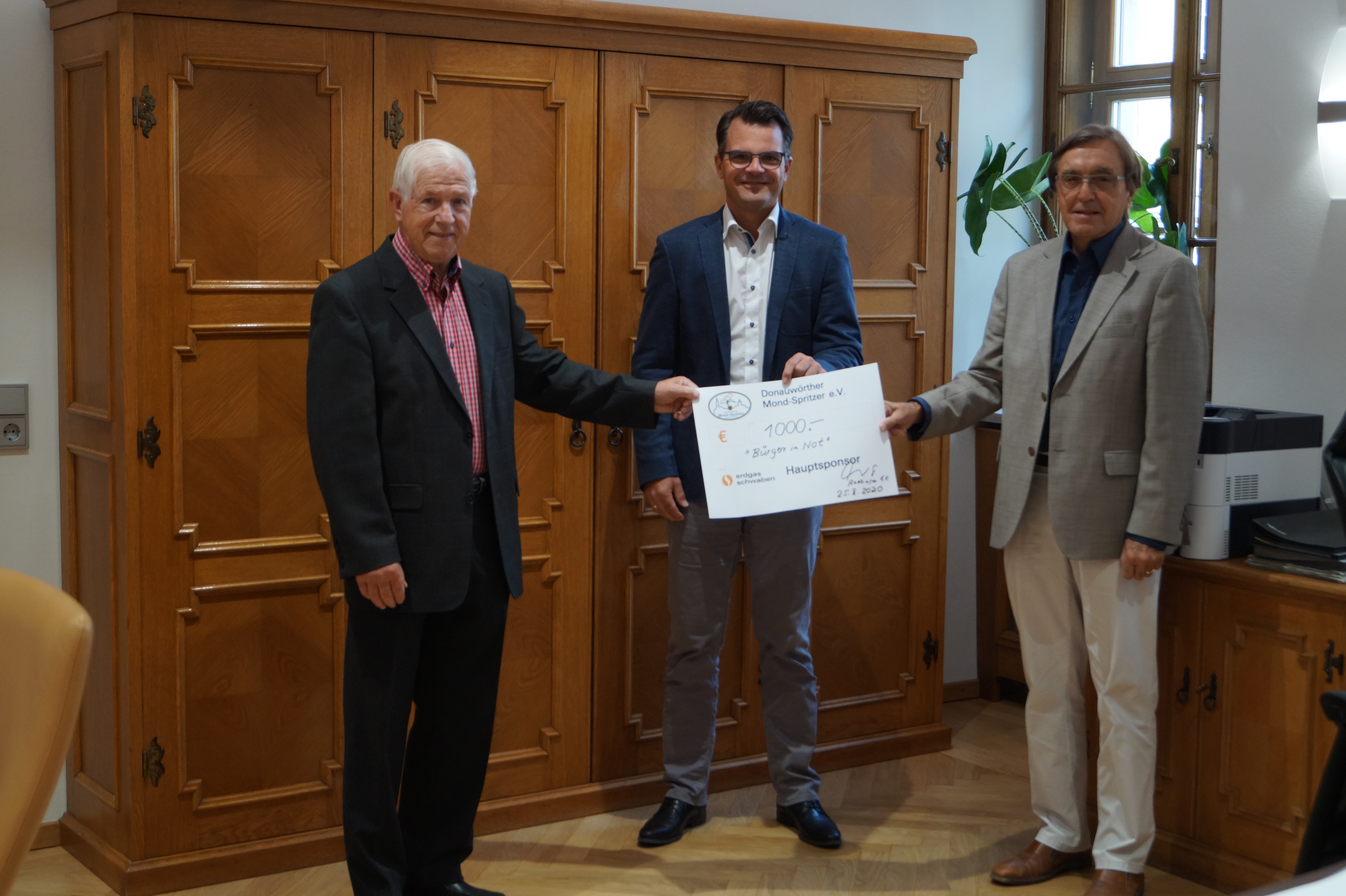 Drei Herren mit Scheck vor Holzschrank