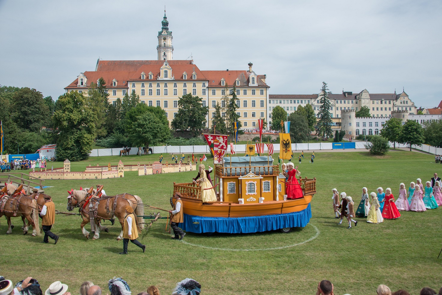 Das Bild zeigt eine Parade von Menschen, die mit barocken Kleidern anzogen sind.