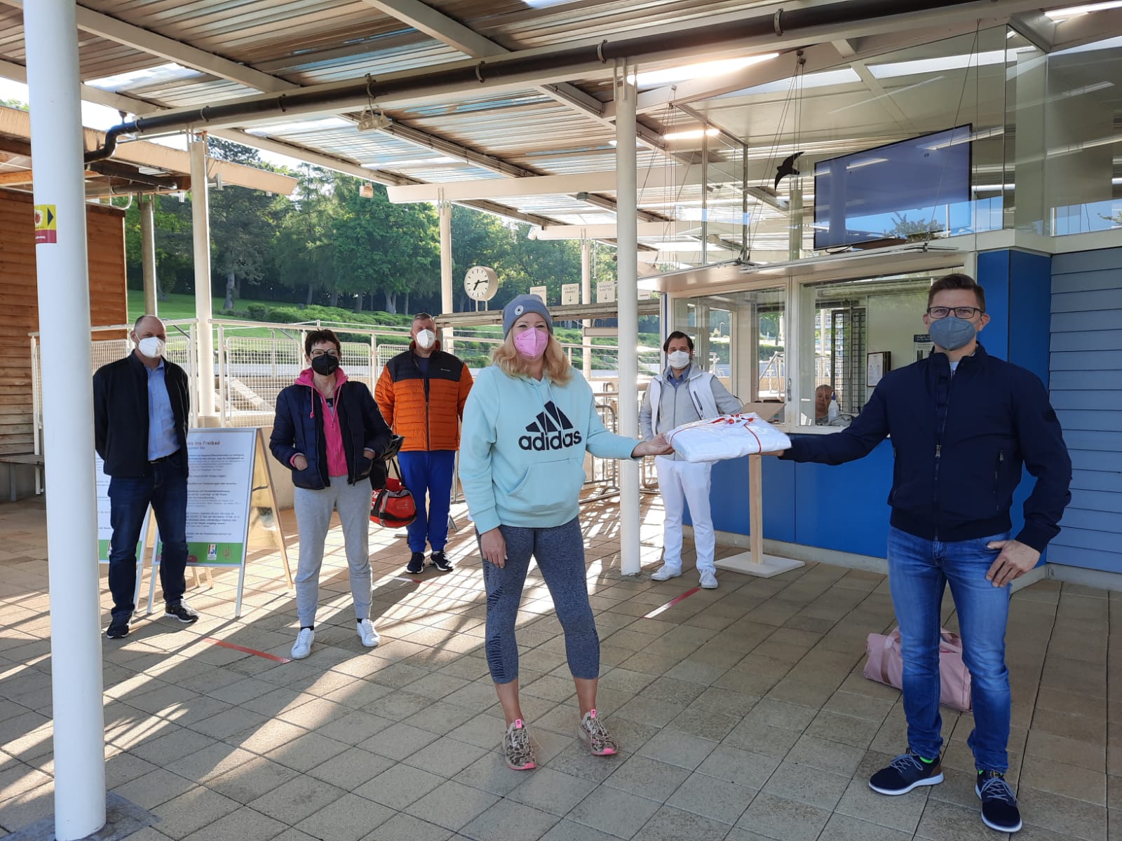 Der Bürgermeister überreicht der ersten Besucherin ein Handtuch. Im Hintergrund sind vier weitere Badegäste zu sehen.