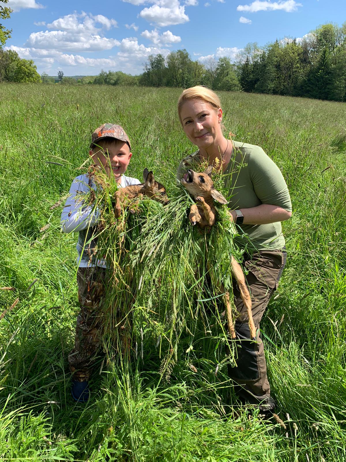 Ein Junge und eine Frau halten zwei Rehkitze in den Händen.