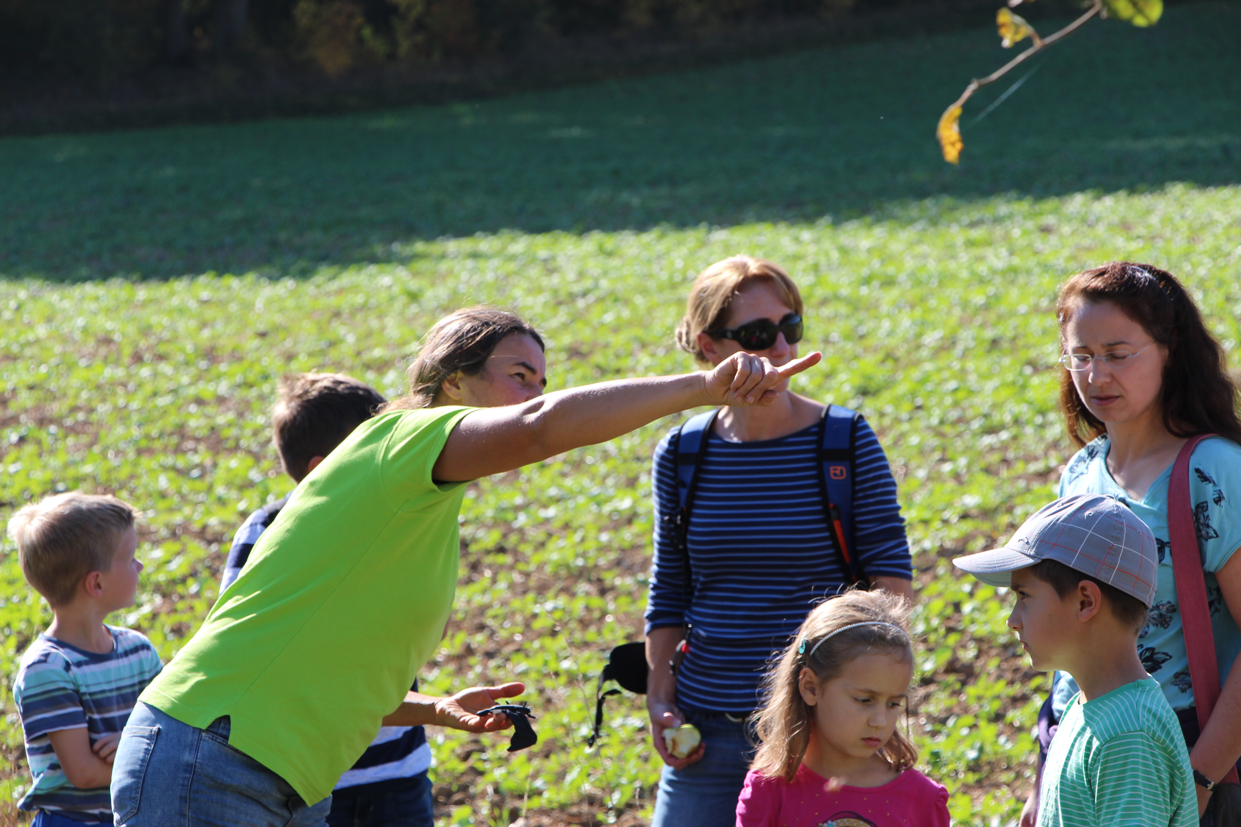 Zu sehen ist eine Frau, welche vor einer Gruppe Menschen mit dem Finger auf etwas in der Natur zeigt.