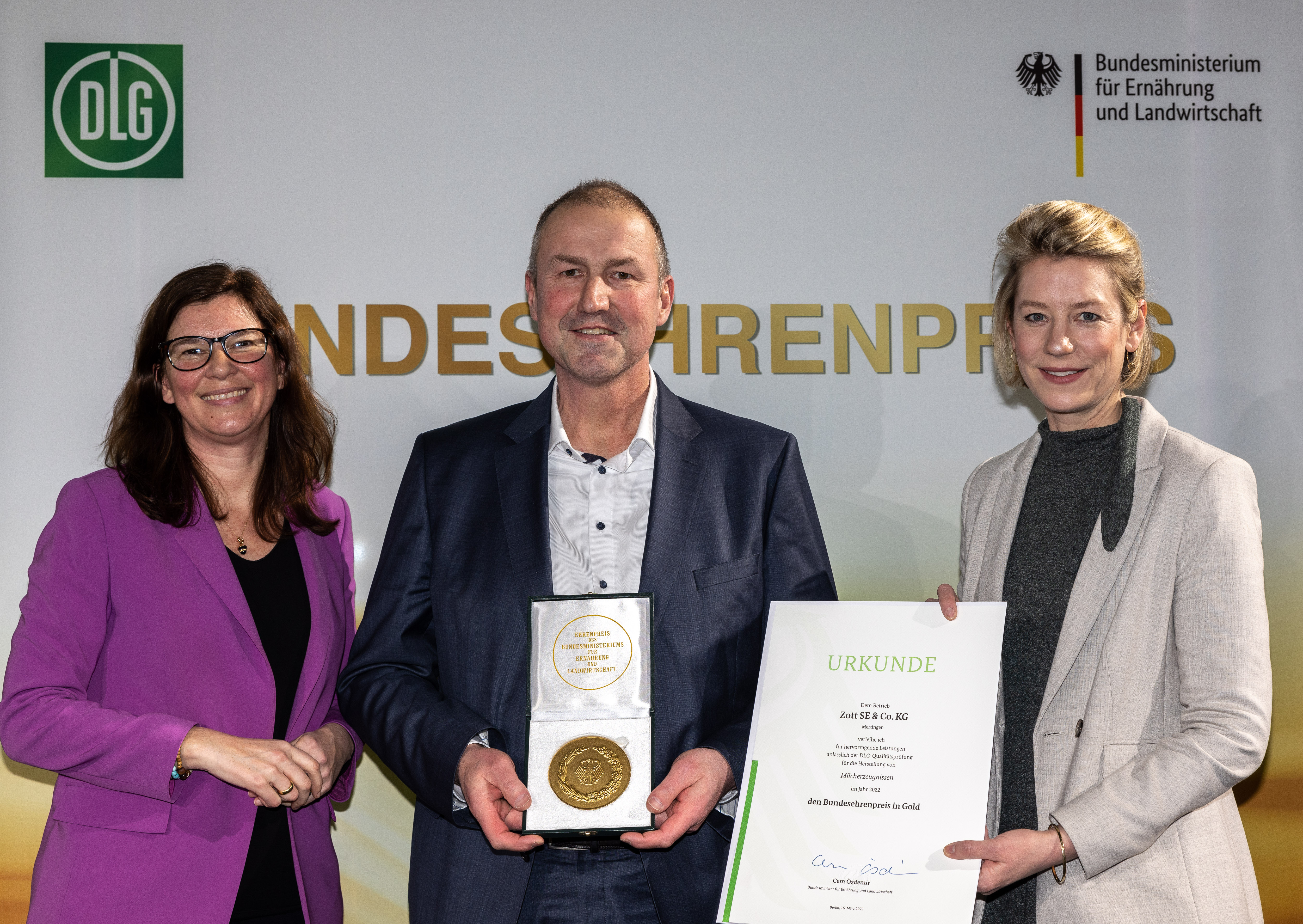 Die Parlamentarische Staatssekretärin Dr. Ophelia Nick (links) überreicht Urkunde und Medaille gemeinsam mit Freya von Czettritz, CEO der DLG-Holding, auf dem 13. Berliner Milchforum an Christian Schramm, Leiter Milcheinkauf bei der Zott SE &amp; Co. KG.