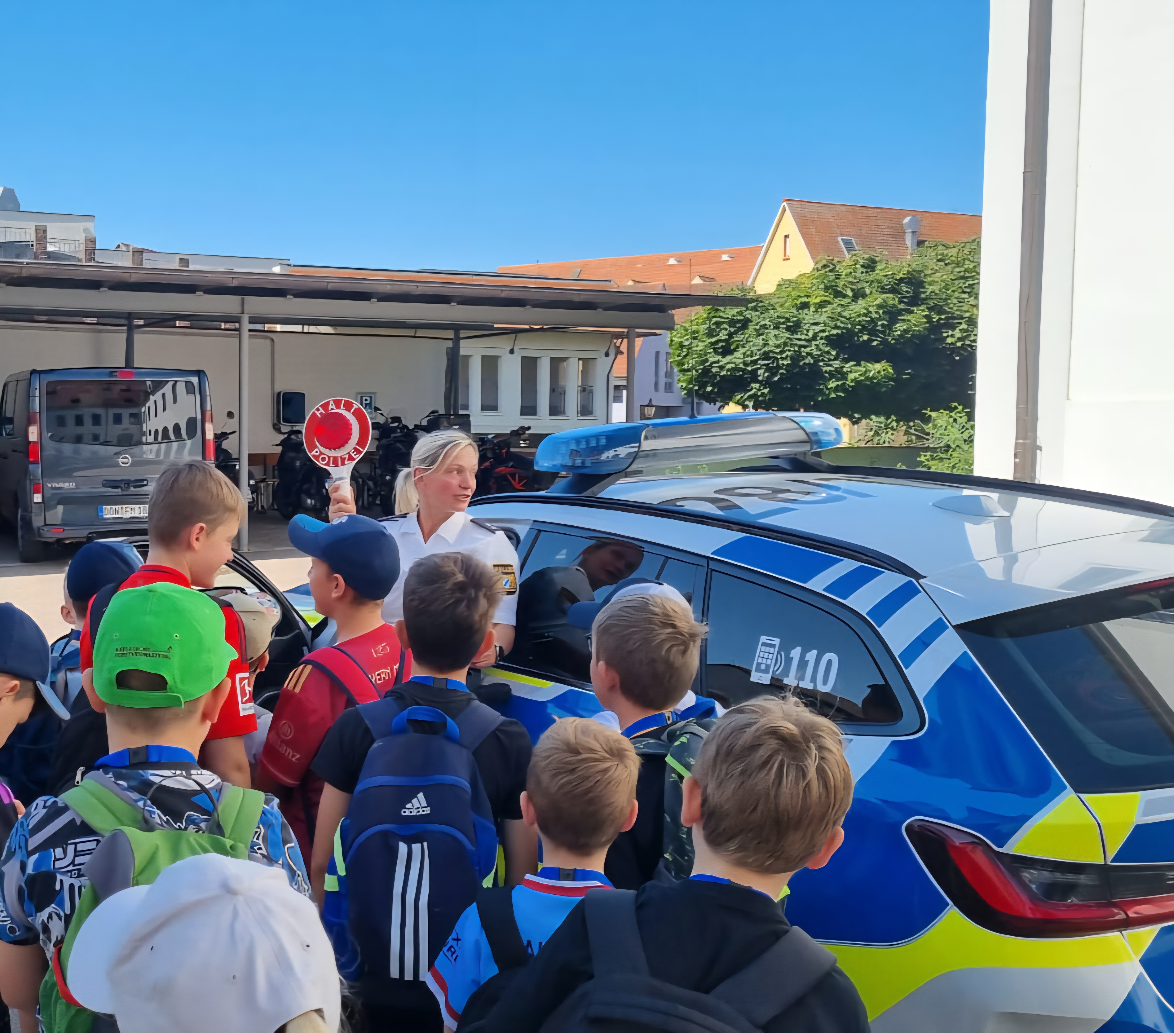 Teilnehmende Kinder und Polizistin Frau Stephanie Mergel vor einem Dienstwagen.