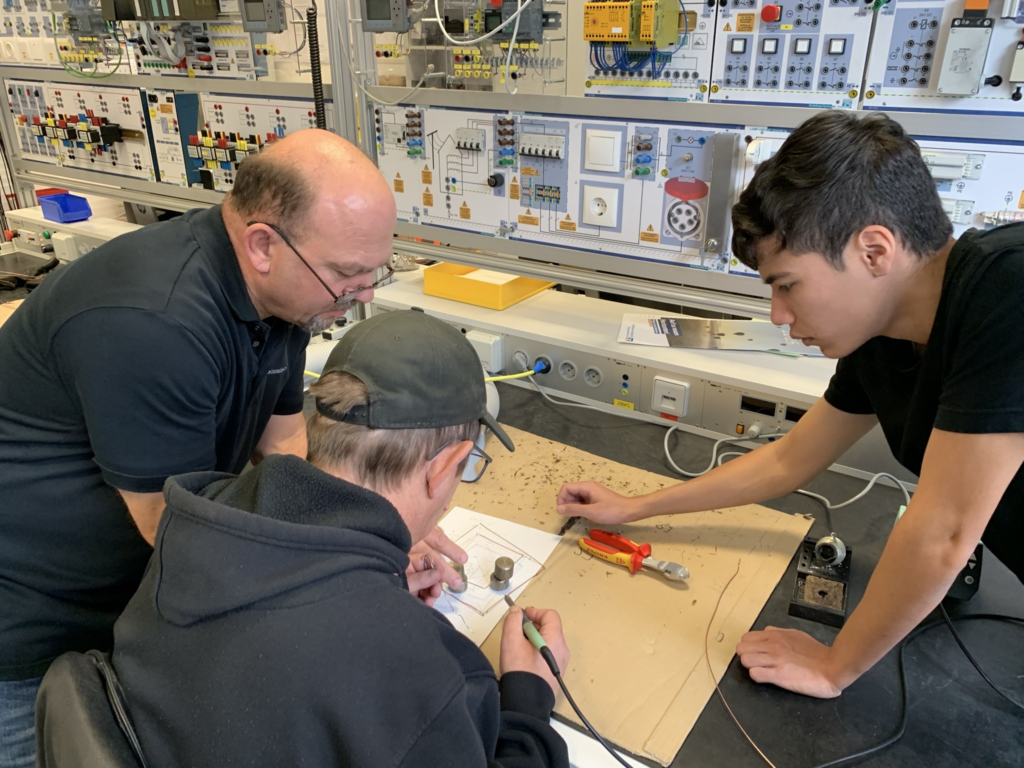 Ein Mitarbeiter aus den Donau-Ries-Werkstätten wird bei Schnupperarbeiten in der Werkstatt der Firma Grenzebach von zwei Kollegen unterstützt.