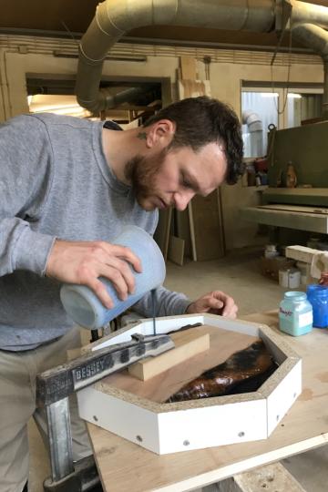 Das Bild zeigt Daniel Bayer, wie er gerade dabei ist, eine Form mit Harz auszugießen.