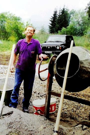 Lachender Mann im lila Poloshirt neben kleinem Betonmischer