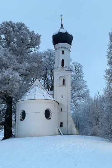 Auf dem Bild ist eine Kapelle in winterlicher Landschaft zu sehen.