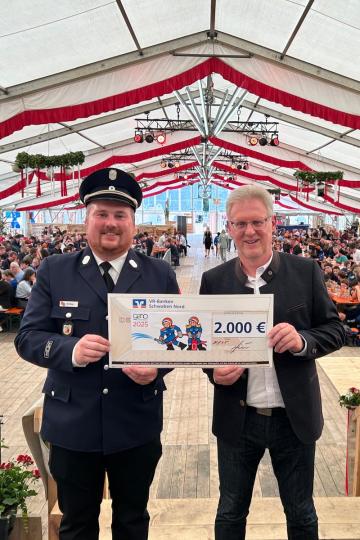 Vorstandsvorsitzender der Raiffeisen-Volksbank Nordschwaben Bernhard Ströbele bei der Spendenübergabe im Festzelt an Kreisjugendwart Markus Meyr.