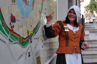 Auf diesem Bild sieht man die Gästeführerin Sonja Fall im historischen Gewand vor einer Karte von Nördlingen.