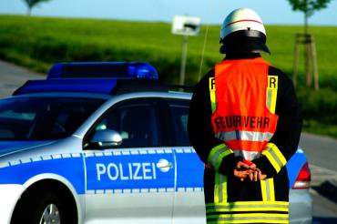 Das Bild zeigt ein Polizeiauto und einen Feuerwehrmann.