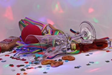 Das Bild zeigt ein Sektglas, Konfetti, einen Klopfer und eine Clownsnase. 