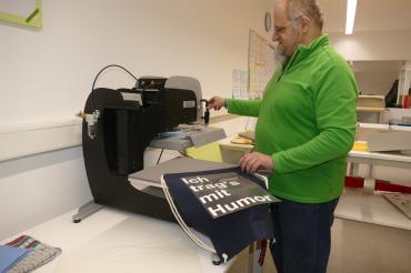 Mitarbeiter Robert Stengl bedruckt an der Thermotransferpresse eigenständig Stoffe.
