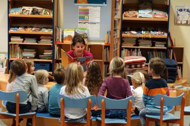 Das Bild zeigt eine Frau beim Vorlesen mit Kindern. 