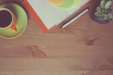 Auf dem Tisch steht eine Kaffeetasse, eine Blume und ein Block. 