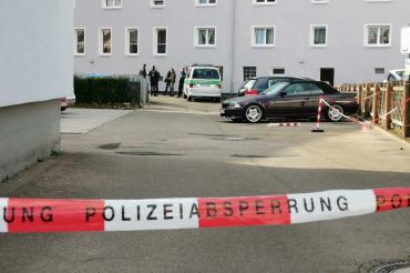 Polizeiabsperrung, im Hintergrund Einsatzkräfte vor einem Wohnblock 