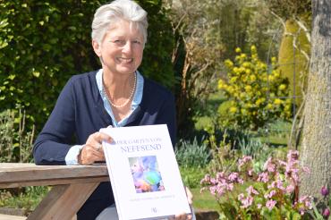 Das Bild zeigt die Autorin mit ihrem Buch in ihrem Garten. 