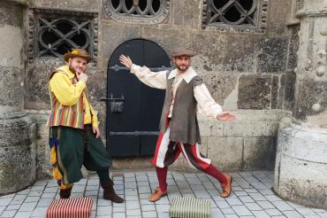 Markant sind nicht nur die Gewänder der beiden sondern auch ihre mitgeführten Schemel, auf die sie sich immer dann stellen, sobald es etwas zu erzählen gibt. 