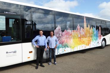 Das Bild zeigt den Künstler Wolfgang Balzer und Verkehrsunternehmer Jörg Schwarzer vor dem Linienbus mit dem Kunstwerk der Nördlinger Stadtsilhouette