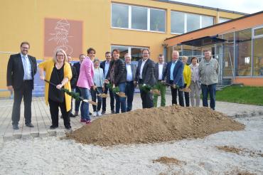 Das Bild zeigt von links nach rechts: Marion Hanrieder, Rektorin; Dr. Bettina Kandler, Architektin;  Michaela Müller, Leiterin der offenen Ganztagsschule; Armin Neudert, Oberbürgermeister und Günther Diethei, Bauunternehmung Eigner, freuen sich beim gemeinsamen Spatenstich mit den anwesenden Stadtratsmitgliedern über das Bauprojekt. 