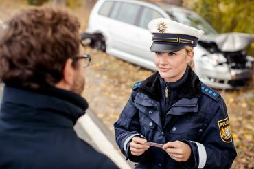 Das Bild zeigt eine Polizistin, die den Ausweis eines Mannes kontrolliert