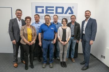 Das Bild zeigt langjährige Mitarbeiter der Firma Geda bei ihrer Ehrung dazu.