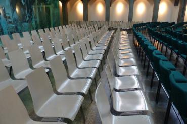 Auf dem Bild zu sehen sind mehrere Stuhlreihen in einer Veranstaltungshalle. 