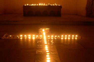 Kerzen bilden ein Kreuz auf dem Boden vor einem Altar