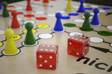 Figuren und Würfel auf einem "Mensch ärgere dich nicht"-Brett