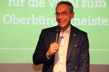 Wolfgang Goschenhofer mit Mikrofon vor einer angestrahlten Leinwand