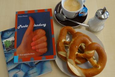 Das Bild zeigt Bücher mit Kaffee und Brezen.