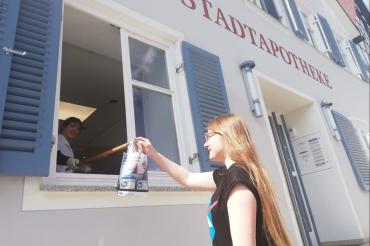 Apothekerin gibt Medikamente durchs Fenster an Kundin