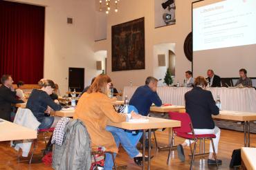 Stadträte sitzen verteilt an Tischen vor Podium