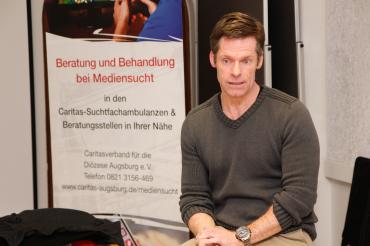 Nils Pruin sitzt neben Banner "Beratung und Behandlung bei Mediensucht"