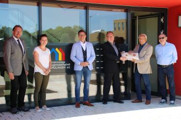 Sechs Personen mit goldenem Schlüssel vor Eingang eines Mehrfamilienhauses