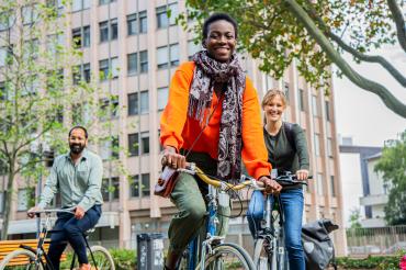 Drei lachende Personen auf Fahrrädern vor Wohnhaus