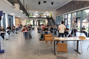 Schüler sitzen an Einzeltischen in Aula, davor eine Lehrkraft