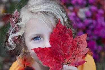 Mädchen mit rotem Ahornblatt vor dem Gesicht
