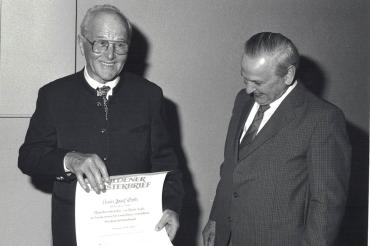 Schwarzweißaufnahme zweier älterer Herren, einer mit Meisterbrief