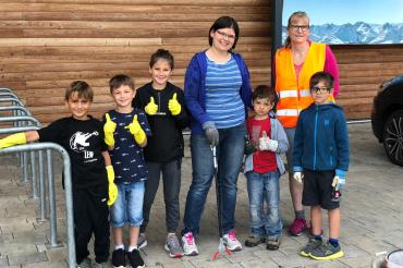 Fünf Kinder und zwei Frauen mit Handschuhen und Müllsammelwerkzeug