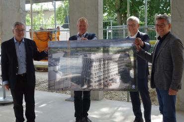 Vier Männer in Rohbau mit großem Bild des Gebäudes