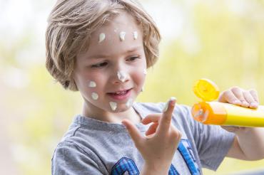 Junge mit Sonnencremetube und Sonnencreme im Gesicht