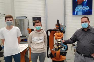 Drei Herren mit Masken und Fertigungsroboter