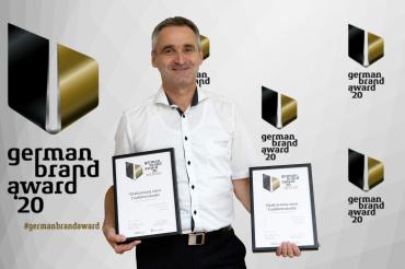 Mann mit zwei Urkunden vor Wand mit Logo "German Brand Award"