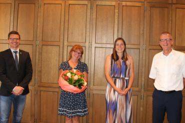 Zwei Männer und zwei Frauen stehen mit Sicherheitsabstand vor holzvertäfelter Wand