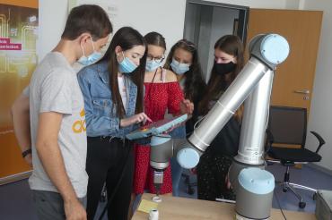 Mädchen mit Schutzmasken lassen sich Roboterarm erklären