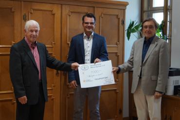 Drei Herren mit Scheck vor Holzschrank