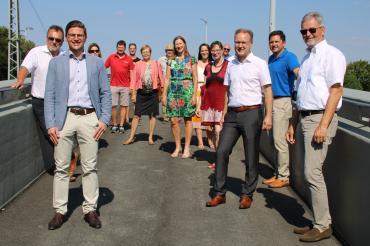 14 Personen stehen mit Abstand auf einer Brücke