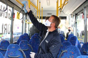 Mann mit Maske trägt Virenschutzschicht auf Haltestange in einem Bus auf