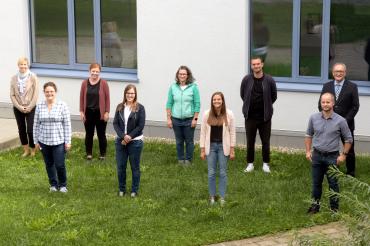 Neun Personen stehen mit Abstand vor Schulgebäude