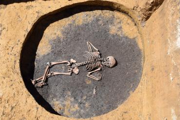 Skelett in kreisrundem, flachem Loch in der Erde